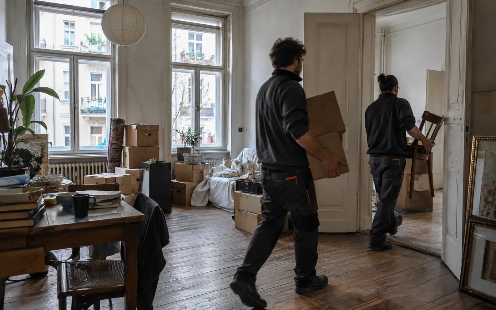 Zwei Mitarbeiter räumen Kartons und Möbel aus einer vollgestellten Altbauwohnung