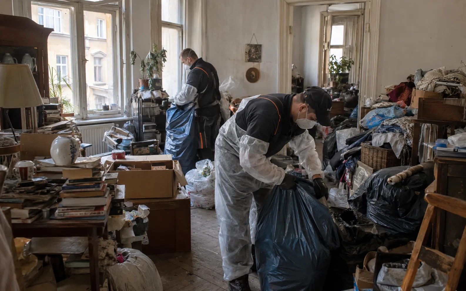 Mitarbeiter mit Schutzausrüstung räumen eine stark vermüllte Wohnung auf