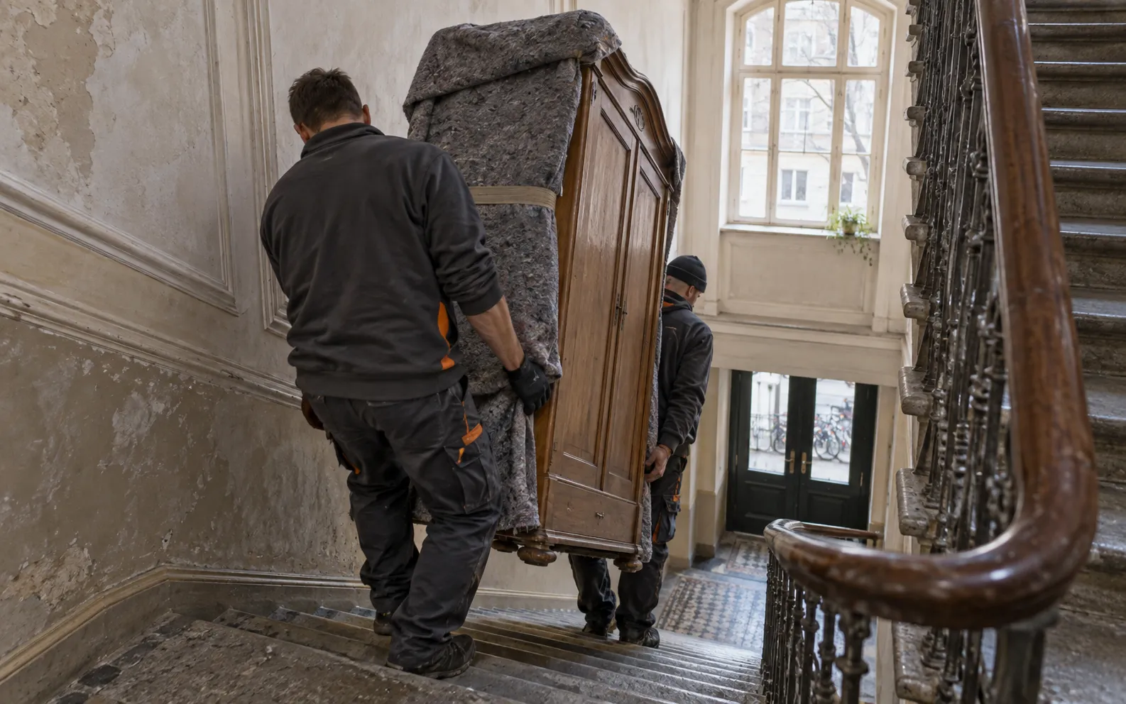 Mitarbeiter tragen einen Schrank durch ein Treppenhaus
