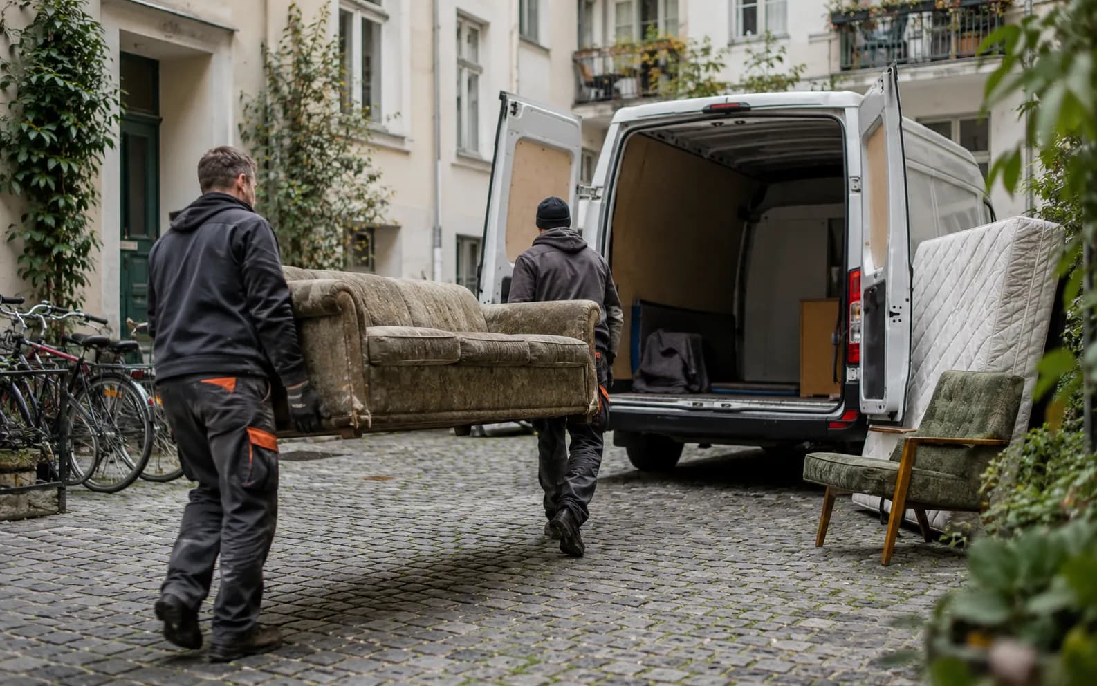 Zwei Mitarbeiter tragen ein Sofa zum Transporter im Innenhof